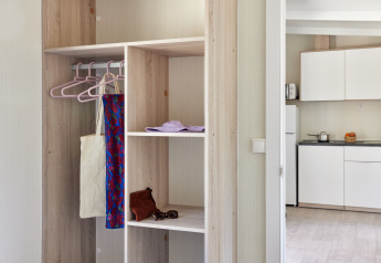 Alojamiento de glamping moderno con armario abierto, perchas y vista parcial de la cocina al fondo.