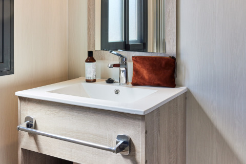 Lavabo moderno de baño con espejo, neceser marrón y bote de jabón en un alojamiento glamping.