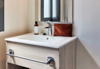 Lavabo moderno de baño con espejo, neceser marrón y bote de jabón en un alojamiento glamping.