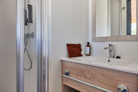 Salle de bain moderne dans un hébergement glamping avec lavabo, miroir, douche et produits de toilette.