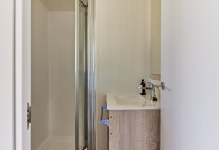 Moderne badkamer bij glamping met douche, wastafel en minimalistisch interieur, gezien door een open deur.