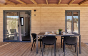 Terraza exterior en alojamiento glamping con pared de madera, mesa de comedor y cuatro sillas bajo techo.