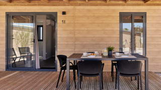 Udendørs terrasse ved glamping-indkvartering med træbeklædning, spisebord og fire stole under overdækning.