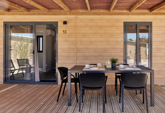 Terraza exterior en alojamiento glamping con pared de madera, mesa de comedor y cuatro sillas bajo techo.