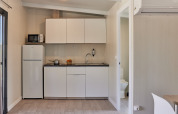 Pequeña cocina glamping con armarios blancos, nevera, microondas y acceso visible al baño.