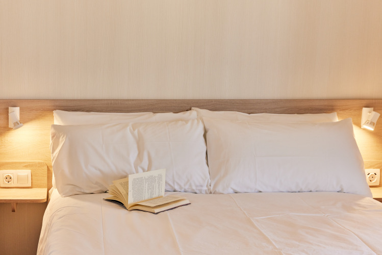 Gemütliches Bett mit weißen Kissen, Leselampen und aufgeschlagenem Buch in luxuriöser Glamping-Unterkunft.