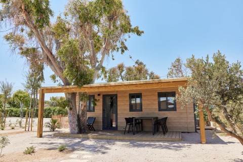 Cabaña llamada Bungalow Premium Ebre con terraza de madera, zona de estar exterior y rodeada de árboles.
