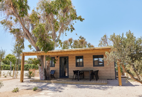 Cabaña llamada Bungalow Premium Ebre con terraza de madera, zona de estar exterior y rodeada de árboles.