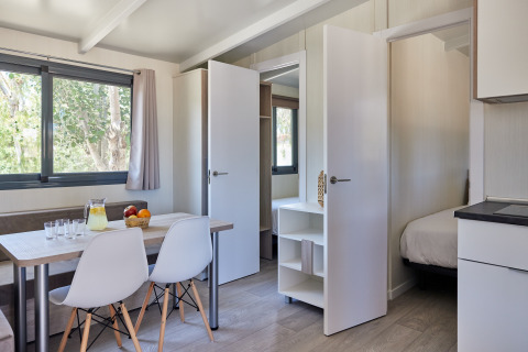 Bright interior of Bungalow Premium Ebre with dining table, chairs, and bedroom view at TAIGA Delta de l'Ebre, Spain.
