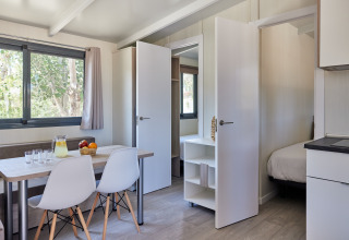 Bright interior of Bungalow Premium Ebre with dining table, chairs, and bedroom view at TAIGA Delta de l'Ebre, Spain.