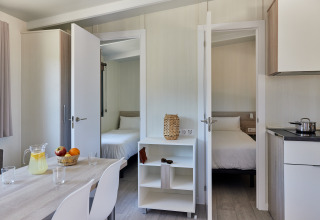 Interior view of Bungalow Premium Ebre at TAIGA Delta de l'Ebre, Spain, showing two bedrooms, kitchen and dining table.