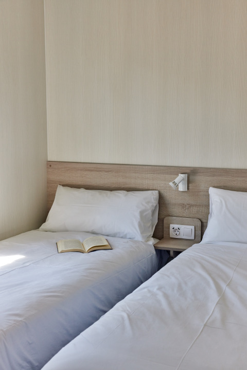 Dos camas individuales con sábanas blancas, un libro sobre una cama en Bungalow Premium Ebre en TAIGA Delta de l'Ebre, España.