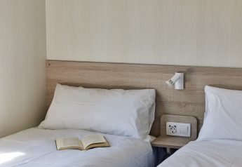 Dos camas individuales con sábanas blancas, un libro sobre una cama en Bungalow Premium Ebre en TAIGA Delta de l'Ebre, España.