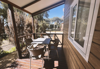 Træveranda med bord og stole på Bungalow Confort Poniente, TAIGA Conil, Spanien, omgivet af træer.