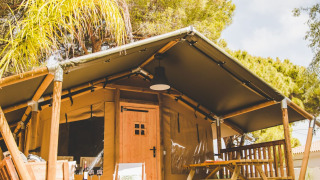 Das Safari-Zelt Glamping Safari Mistral mit Holzveranda und Picknickbank in einem waldreichen Gebiet.