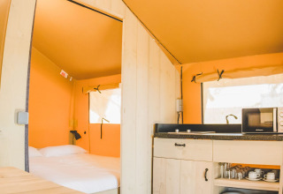 Interior de la tienda Glamping Safari Mistral en TAIGA Conil, España, con cama y pequeña cocina.