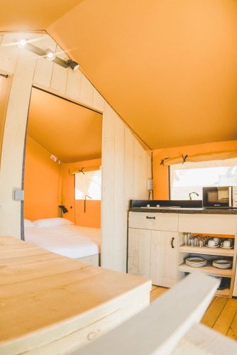Innenraum des Safari-Zelts Glamping Safari Mistral bei TAIGA Conil, Spanien, mit Bett und Küchenzeile.