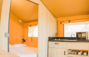 Interior de la tienda Glamping Safari Mistral en TAIGA Conil, España, con cama y pequeña cocina.
