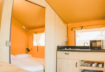 Intérieur de la tente Glamping Safari Mistral à TAIGA Conil, Espagne, avec lit et coin cuisine.