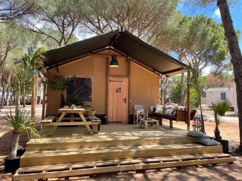 Tienda safari Glamping Safari Siroco Premium en TAIGA Conil, España, con terraza de madera y asientos exteriores.