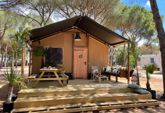 Tienda safari Glamping Safari Siroco Premium en TAIGA Conil, España, con terraza de madera y asientos exteriores.