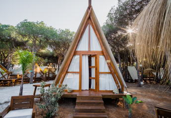 Glamping Tipi Almadraba, tente tipi moderne en bois et toile, entourée d’arbres et de mobilier extérieur.