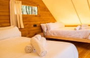 Innenraum eines Glamping-Safari-Zeltes mit zwei Betten, Holzverkleidung und gerollten Handtüchern.