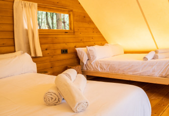 Interior de tienda glamping tipi en TAIGA Conil, España, con dos camas, paredes de madera y toallas.