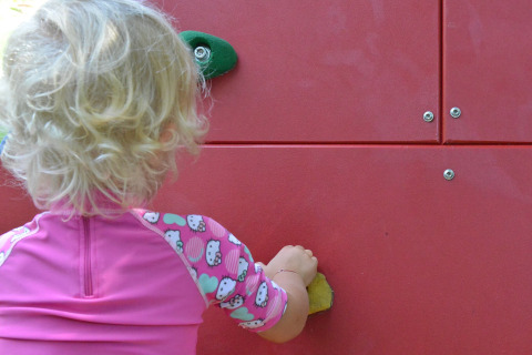 Klein kindje met roze outfit klimt op een rode wand bij Drau Camping Sachsenburg, Karinthië, Oostenrijk.