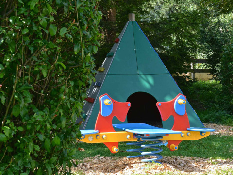 Spielplatz im Drau Camping Sachsenburg, Kärnten, mit bunter Wippe und grünem Tipi-Zelt.