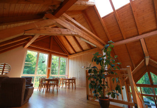 Intérieur d’un chalet en bois à Drau Camping Sachsenburg avec de grandes fenêtres et poutres apparentes.