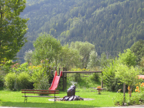 Parque infantil con tobogán rojo y banco entre vegetación, en un parque vacacional en Carintia, Austria.