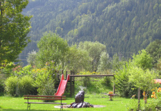 Parque infantil con tobogán rojo y banco entre vegetación, en un parque vacacional en Carintia, Austria.
