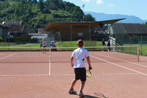 Un niño juega al tenis en una cancha exterior en Drau Camping Sachsenburg, un parque vacacional en Carintia, Austria.