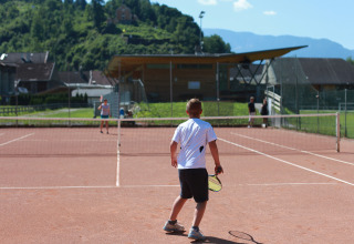 Et barn spiller tennis på udendørsbanen ved Drau Camping Sachsenburg feriepark i Carinthia, Østrig.