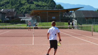 Un niño juega al tenis en una cancha exterior en Drau Camping Sachsenburg, un parque vacacional en Carintia, Austria.