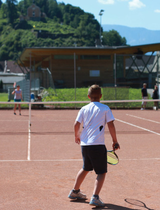 Ein Kind spielt Tennis auf dem Außenplatz im Drau Camping Sachsenburg Ferienpark in Kärnten, Österreich.
