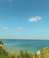 Paysage côtier près de Quiberville, Normandie, France avec falaises herbeuses, mer bleue et ciel dégagé.