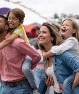 Happy parents giving piggyback rides to their children at a glamping holiday park with colorful tents.