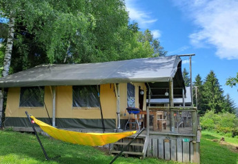 Tienda safari Base Lodge en Camping Les Sapins en Francia, con hamaca amarilla y césped verde.
