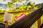 Une personne lit un livre dans un hamac Fatboy à la tente safari Base Lodge, Camping Les Sapins, France.