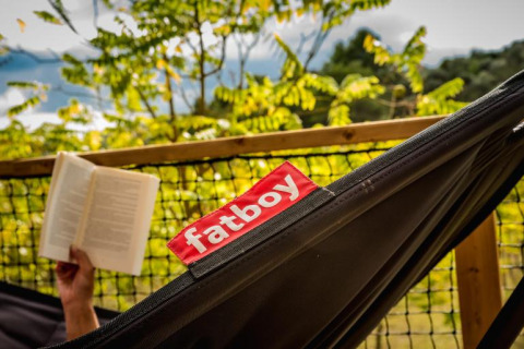Person liest ein Buch in einer Fatboy-Hängematte im Safari-Zelt Base Lodge, Camping Les Sapins, Frankreich.
