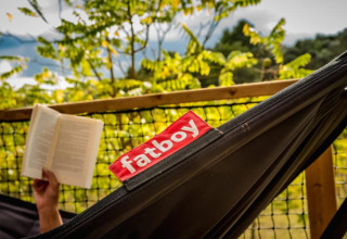 Persona leyendo un libro en una hamaca Fatboy en la tienda safari Base Lodge de Camping Les Sapins, Francia.