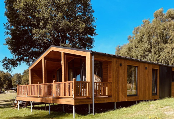 Moderne træhytte med stor veranda ved Lakehouse Scandi, Wilsumer Berge, Tyskland, omgivet af natur.