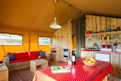Interior of a safari tent with rustic wood furniture, cozy sofa, small kitchen, and dining table.
