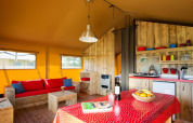 Interior de tienda safari con muebles rústicos de madera, sofá, cocina pequeña y mesa de comedor.