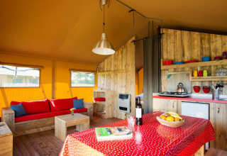 Interno di una tenda safari con mobili in legno rustico, divano, angolo cucina e tavolo da pranzo.