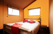 Habitación acogedora en tienda safari con cama de madera, ropa de cama blanca y detalles rojos.
