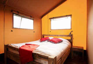 Habitación acogedora en tienda safari con cama de madera, ropa de cama blanca y detalles rojos.