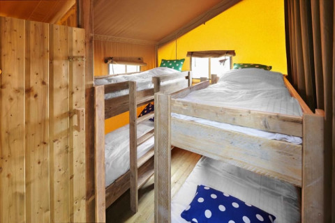 Interior of a safari tent featuring four wooden bunk beds, white bedding, and colorful pillows.